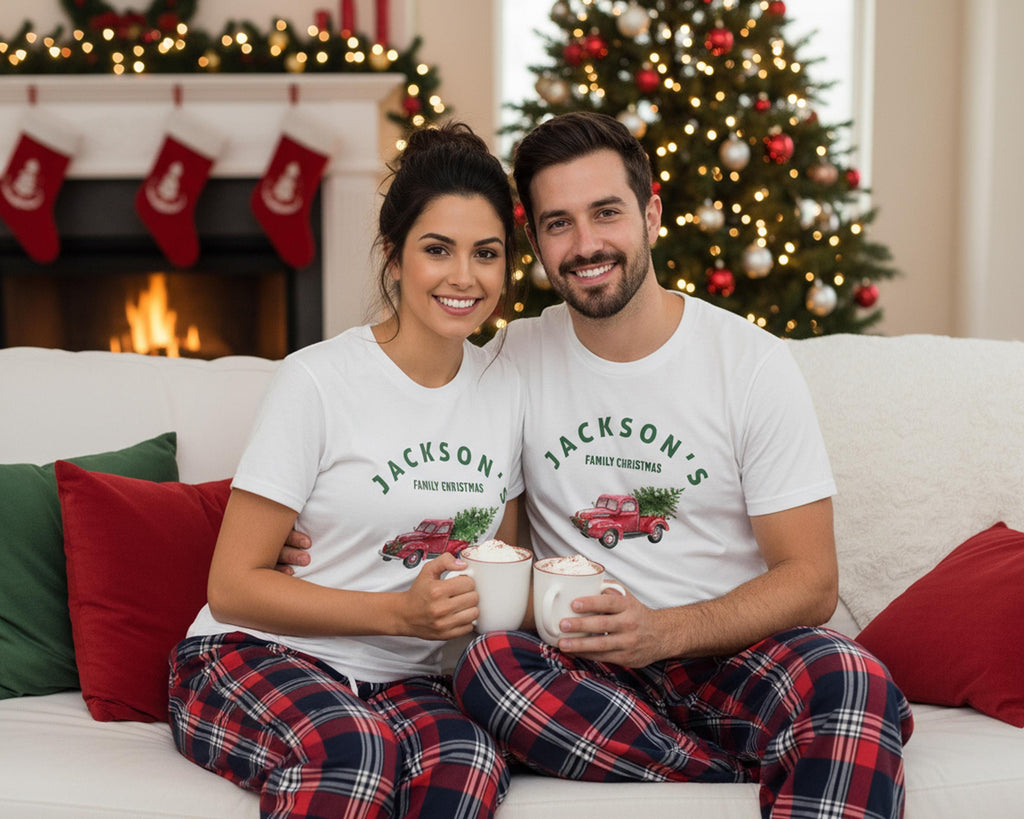 A couple wearing matching white t-shirts with a Christmas tree graphic and the text "JACKSON'S FAMILY CHRISTMAS" sits on a couch, smiling and holding cups of coffee.