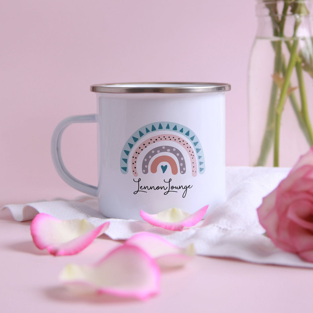 A white ceramic mug with a colorful rainbow design and the text "Lennon Lounge" printed on it, placed on a pink surface with pink rose petals around it.