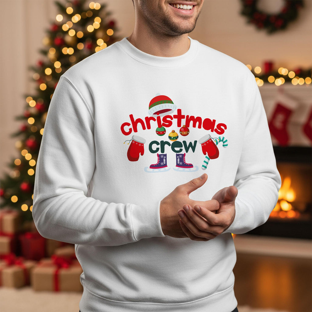 A man wearing a white sweater with a Christmas crew design on it, smiling and standing in front of a Christmas tree.