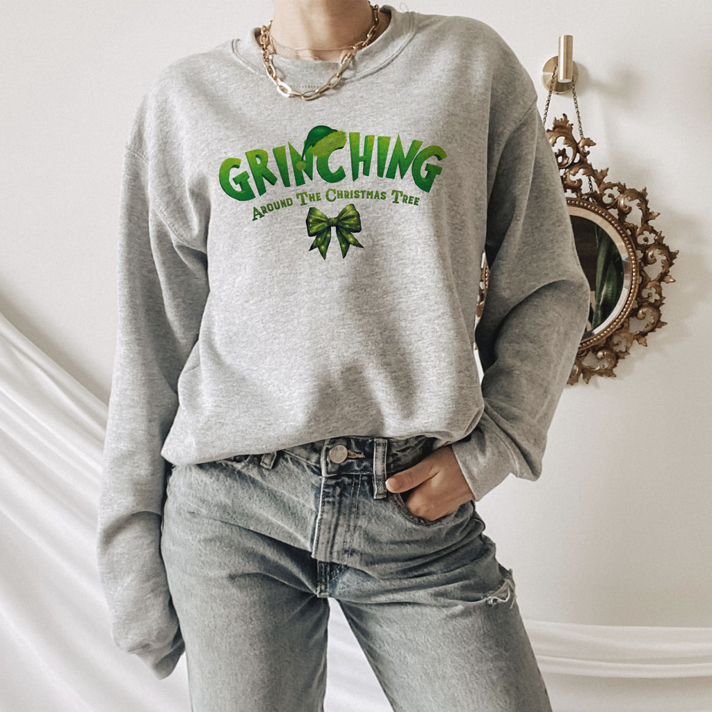 A person wearing a gray sweatshirt with a green graphic and text, standing in front of a mirror and a wall with a decorative piece.