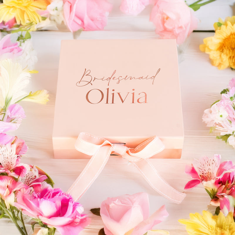 a pink box with a ribbon around it and flowers around it