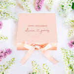 a pink box with a pink ribbon on top of flowers