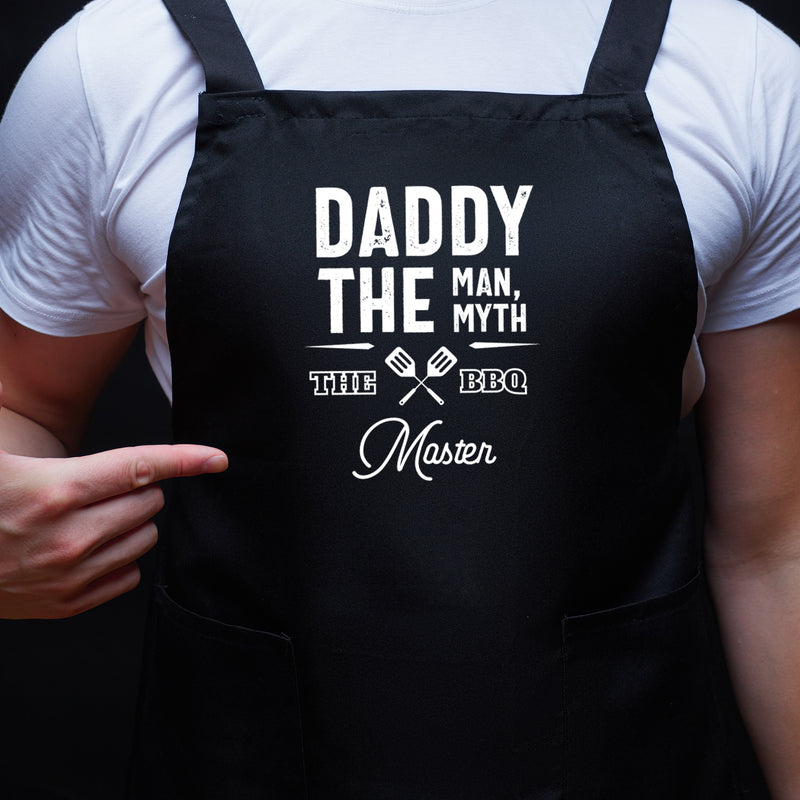 a man wearing a black apron that says daddy the man, the myth, the