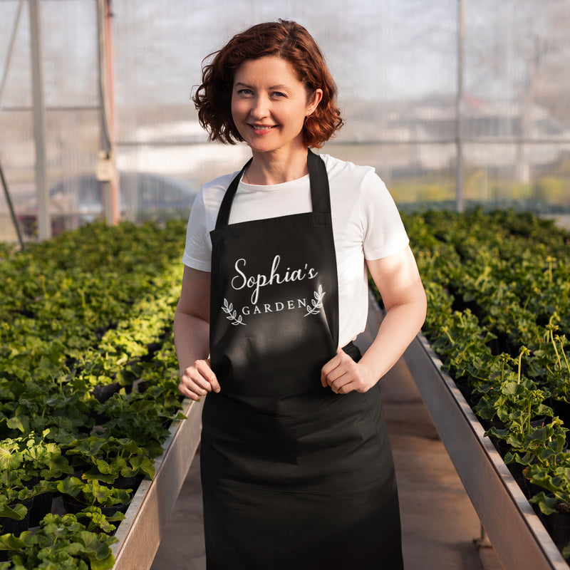 a woman standing in a greenhouse holding a black apron