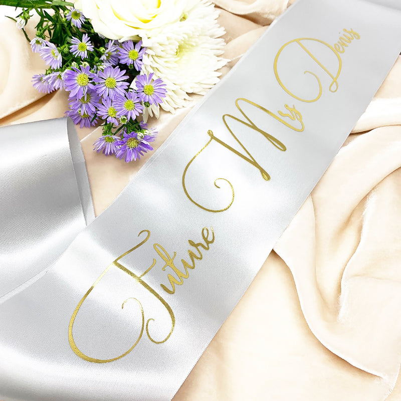 a white sash with a name on it next to a bouquet of flowers