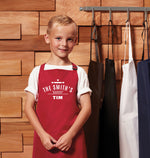 a young boy wearing a red apron standing in front of a wooden wall