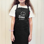 a young girl wearing a black apron with the words sous chef on it